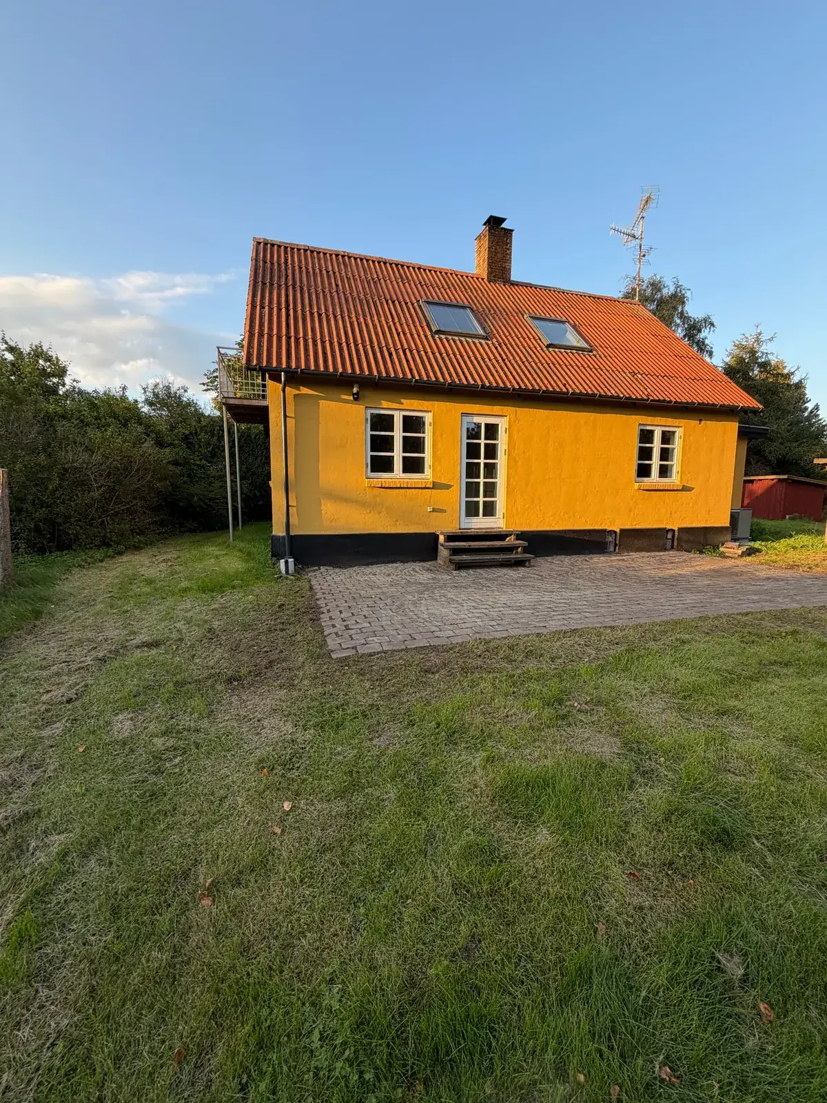 Gul facade med rødt tegltag og ny terrasse efter renoveringen